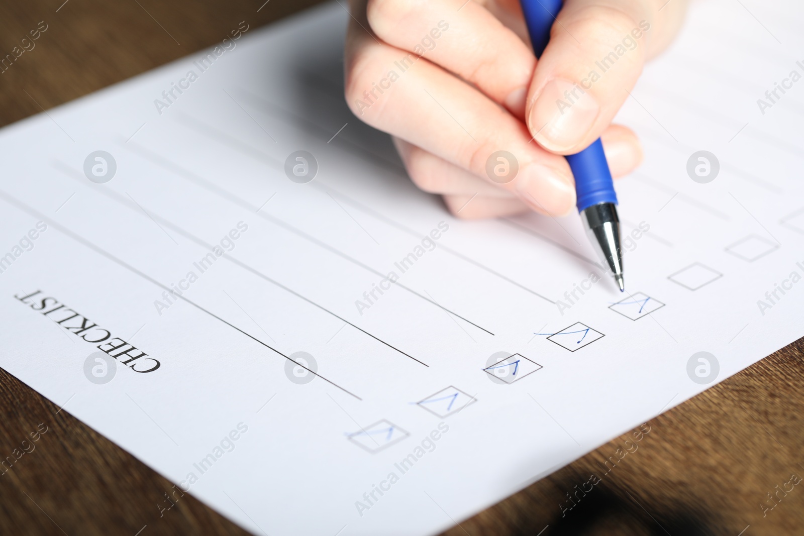 Photo of Woman checking box of paper form at wooden table, closeup