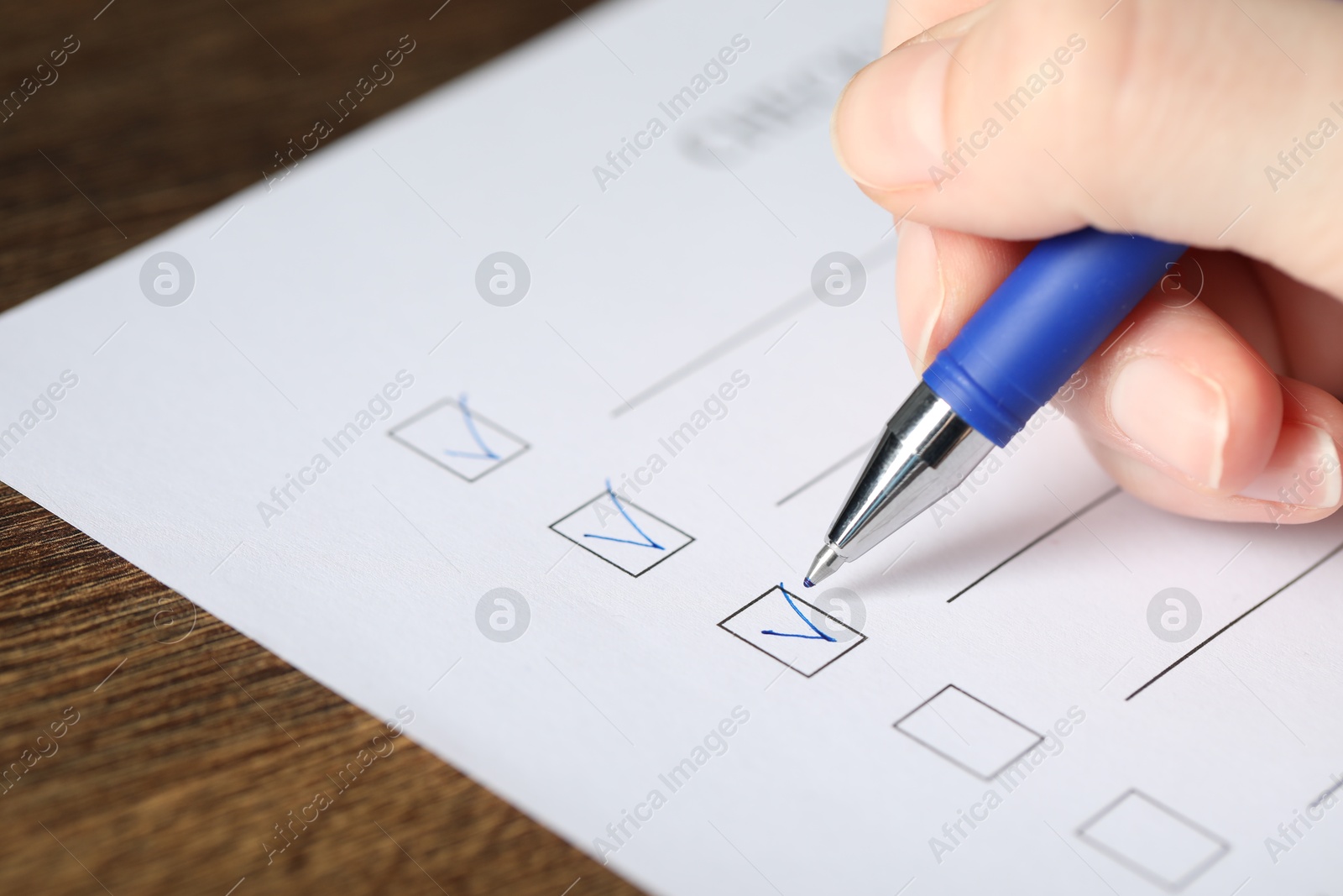 Photo of Woman checking box of paper form at wooden table, closeup