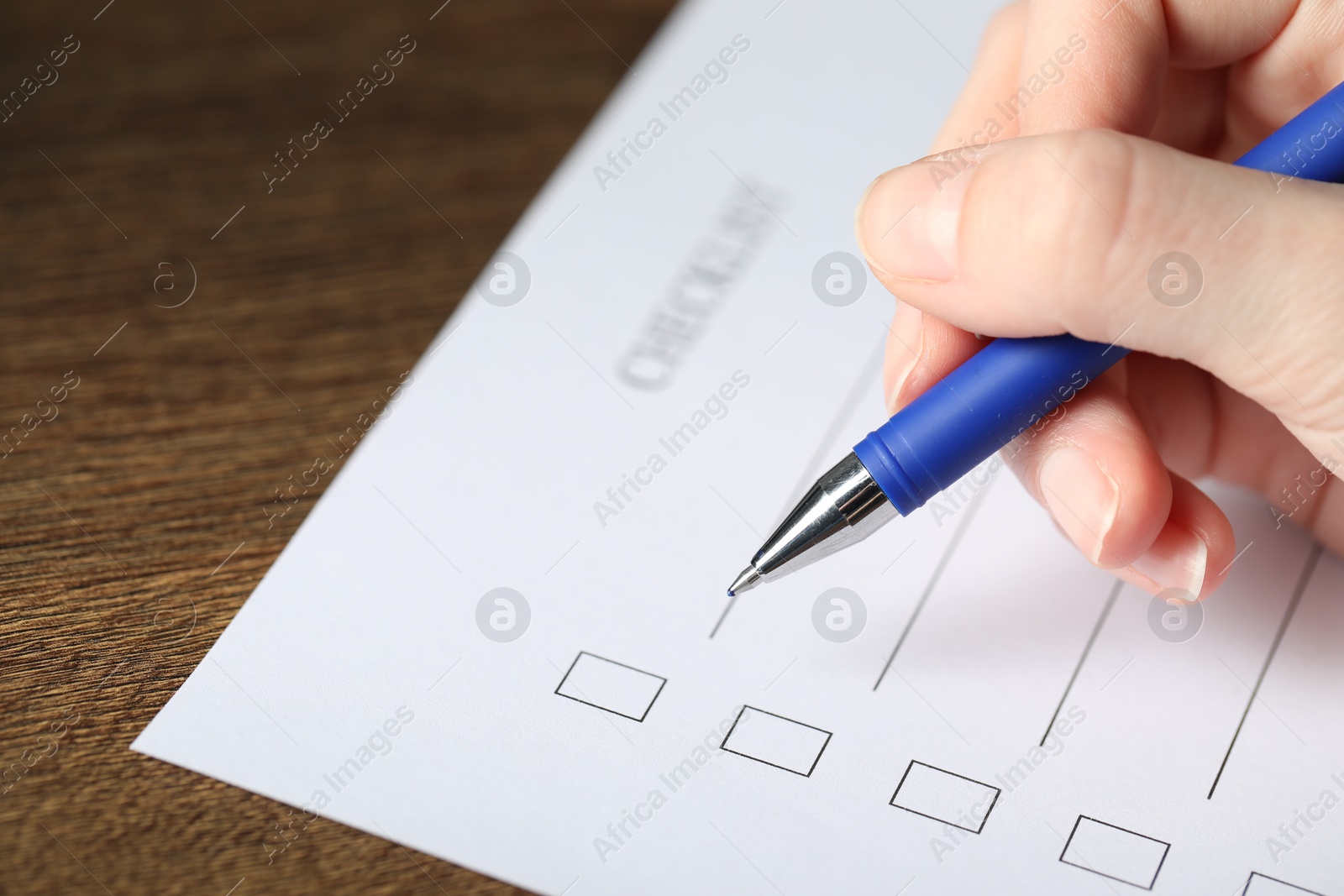 Photo of Woman checking box of paper form at wooden table, closeup