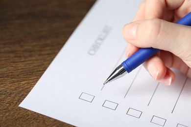 Photo of Woman checking box of paper form at wooden table, closeup