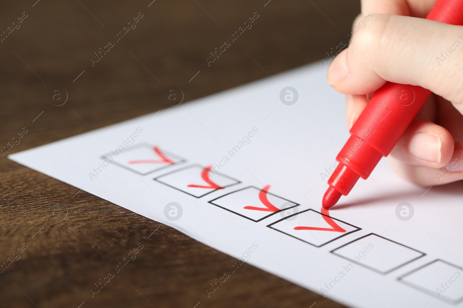 Photo of Woman checking box of paper form at wooden table, closeup