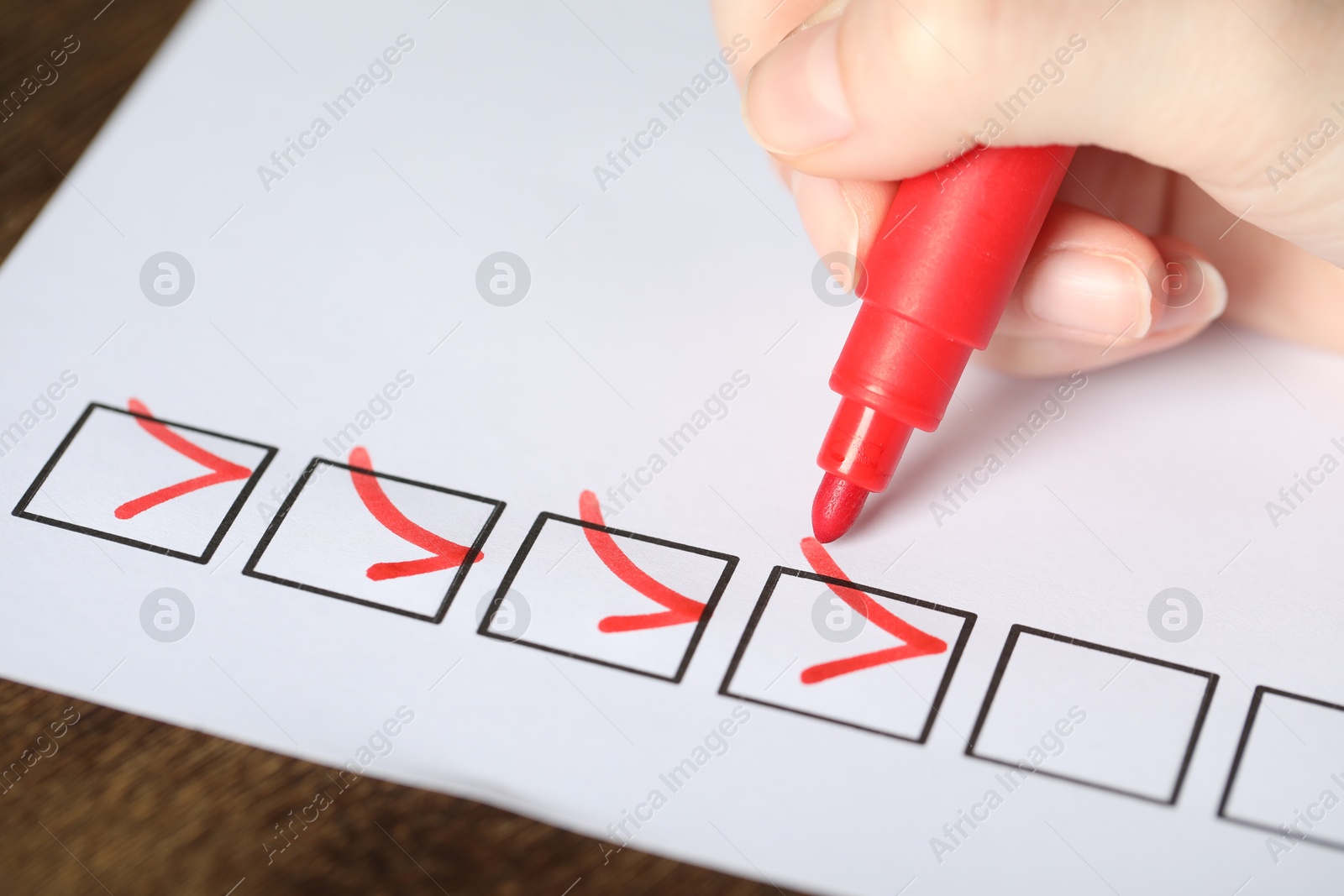 Photo of Woman checking box of paper form at wooden table, closeup