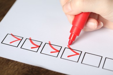 Photo of Woman checking box of paper form at wooden table, closeup