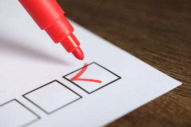 Photo of Paper sheet with checkboxes and red marker at wooden table, closeup