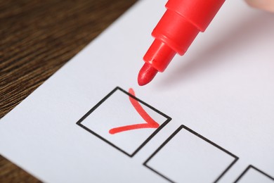 Photo of Paper sheet with checkboxes and red marker at wooden table, closeup