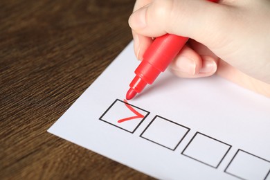 Photo of Woman checking box of paper form at wooden table, closeup