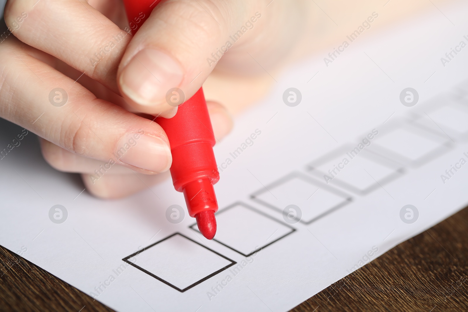 Photo of Woman checking box of paper form at wooden table, closeup