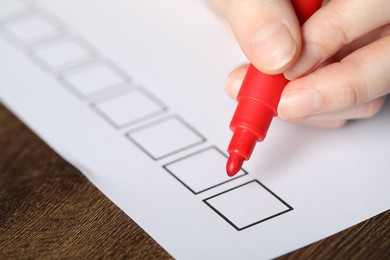 Photo of Woman checking box of paper form at wooden table, closeup