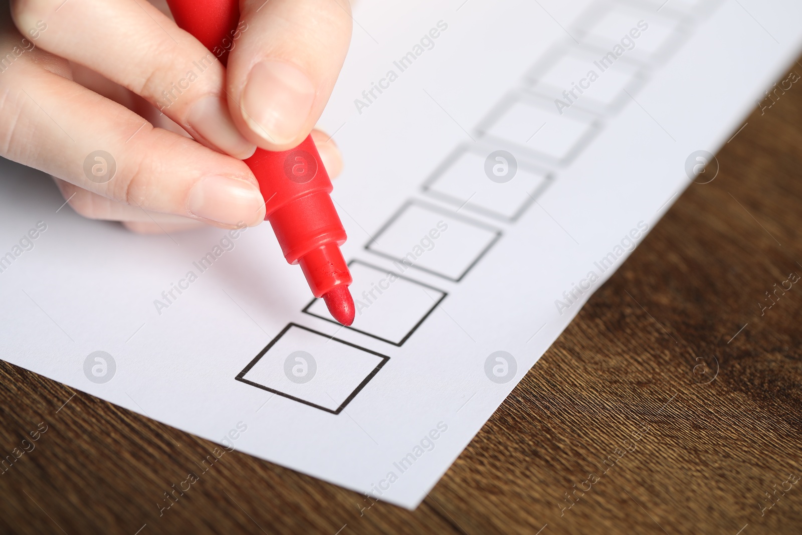 Photo of Woman checking box of paper form at wooden table, closeup