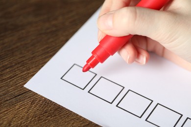 Photo of Woman checking box of paper form at wooden table, closeup