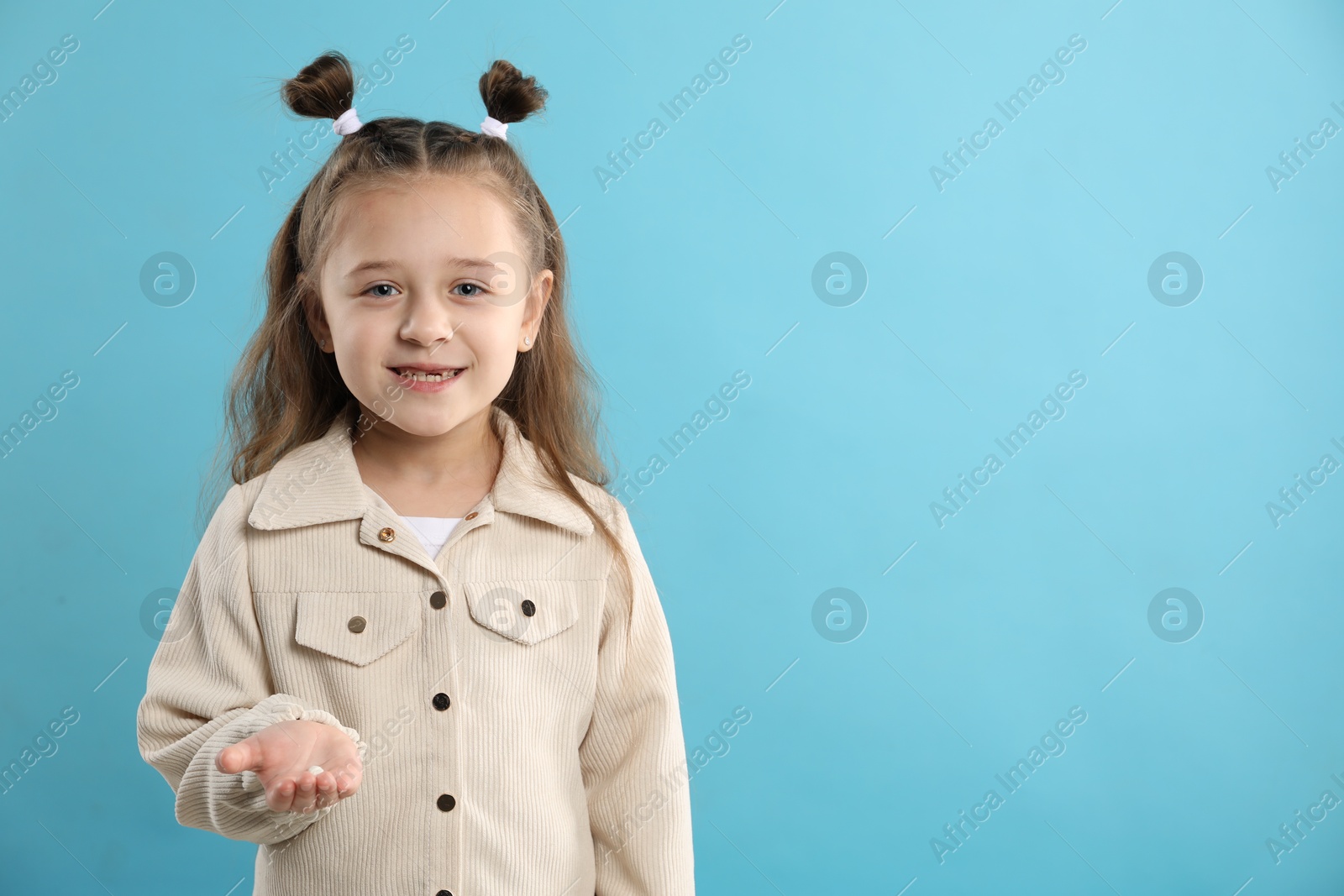 Photo of Cute little girl with missing tooth on light blue background, space for text. Waiting for tooth fairy