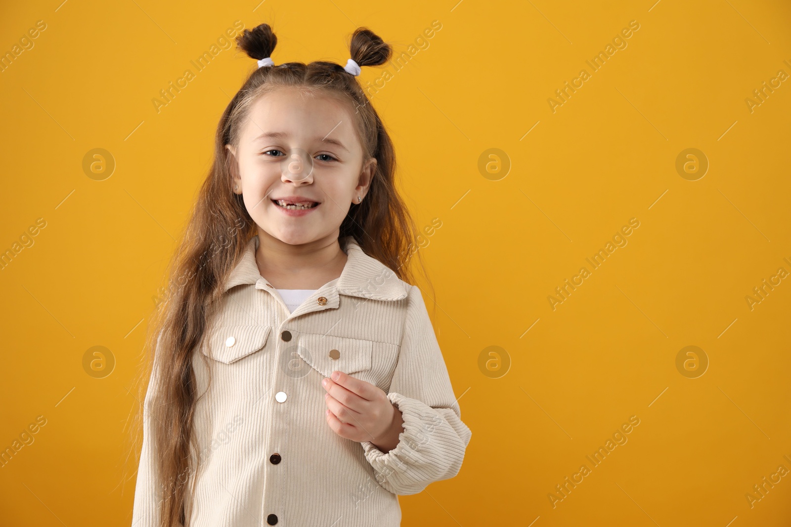 Photo of Cute little girl with missing tooth on orange background, space for text. Waiting for tooth fairy