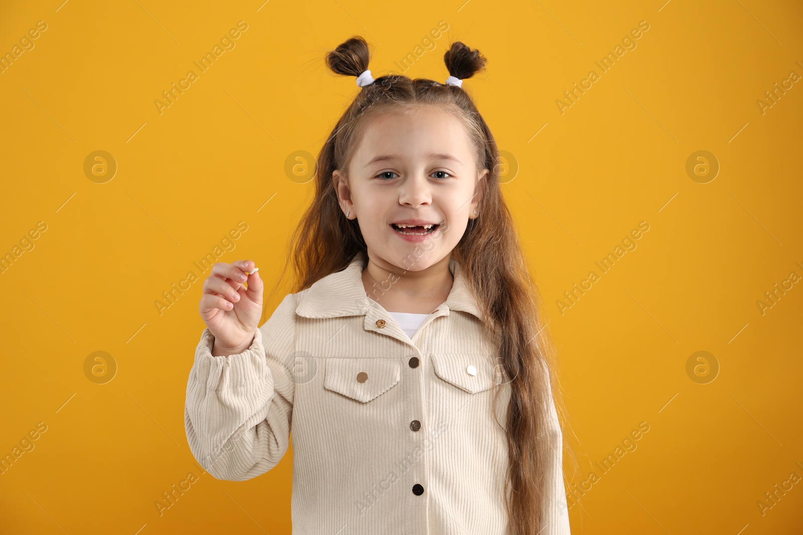 Photo of Cute little girl with missing tooth on orange background. Waiting for tooth fairy