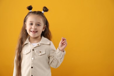 Photo of Cute little girl with missing tooth on orange background, space for text. Waiting for tooth fairy