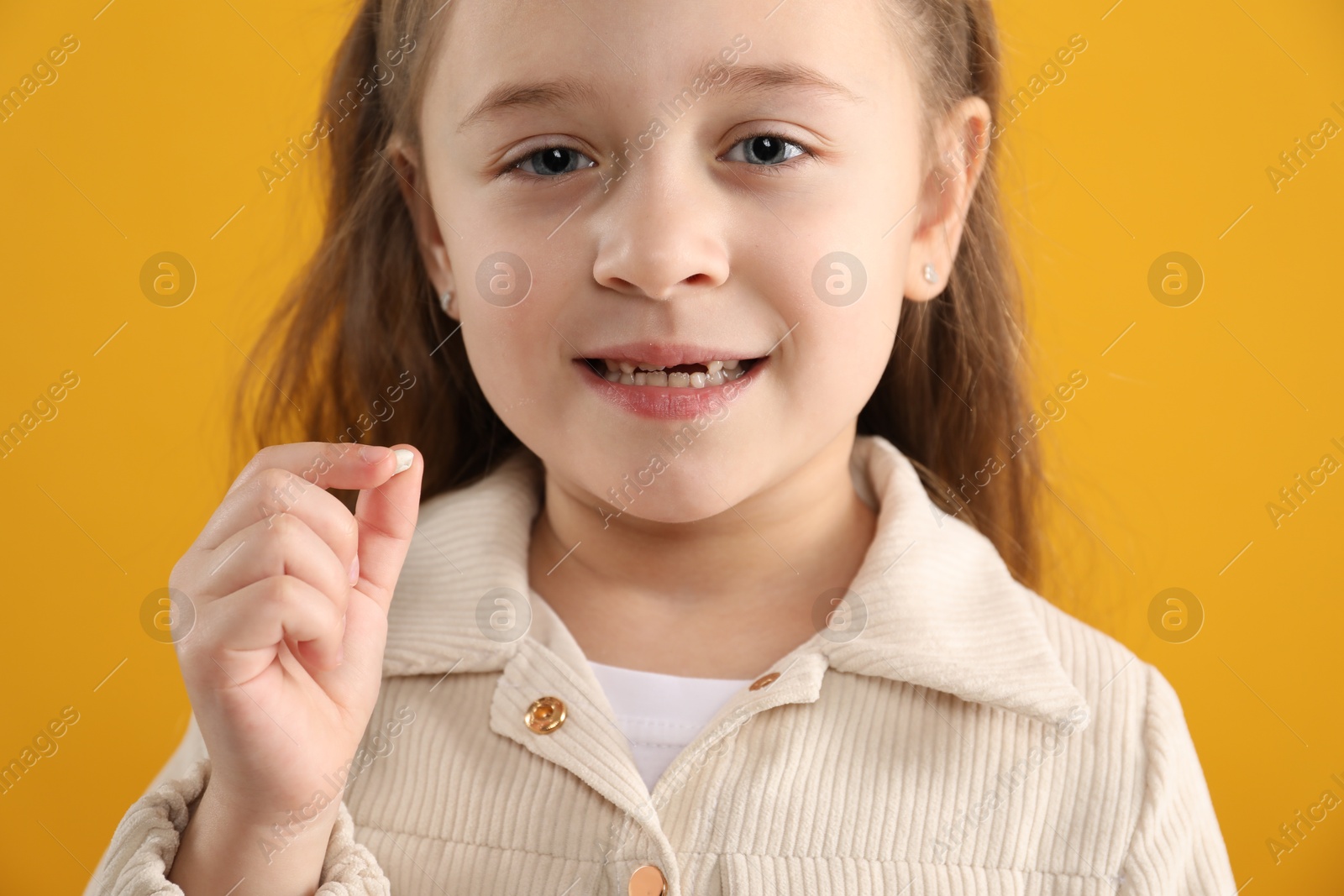 Photo of Cute little girl with missing tooth on orange background, closeup. Waiting for tooth fairy