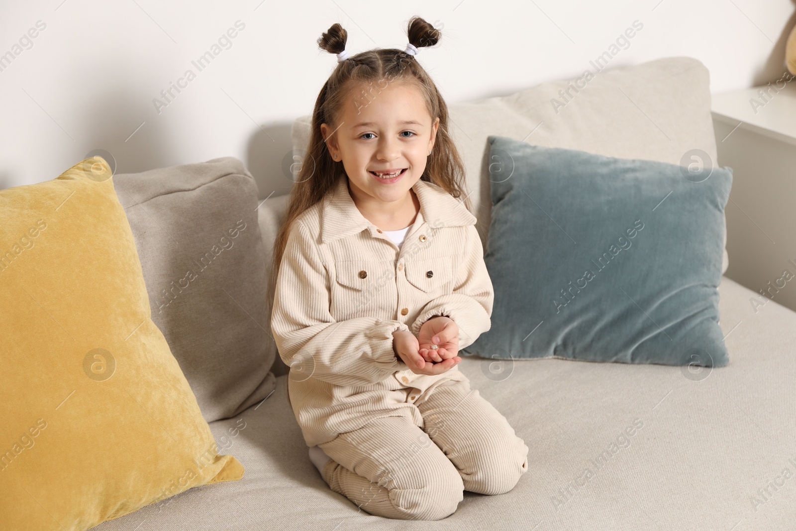 Photo of Cute little girl with missing tooth on sofa indoors. Waiting for tooth fairy