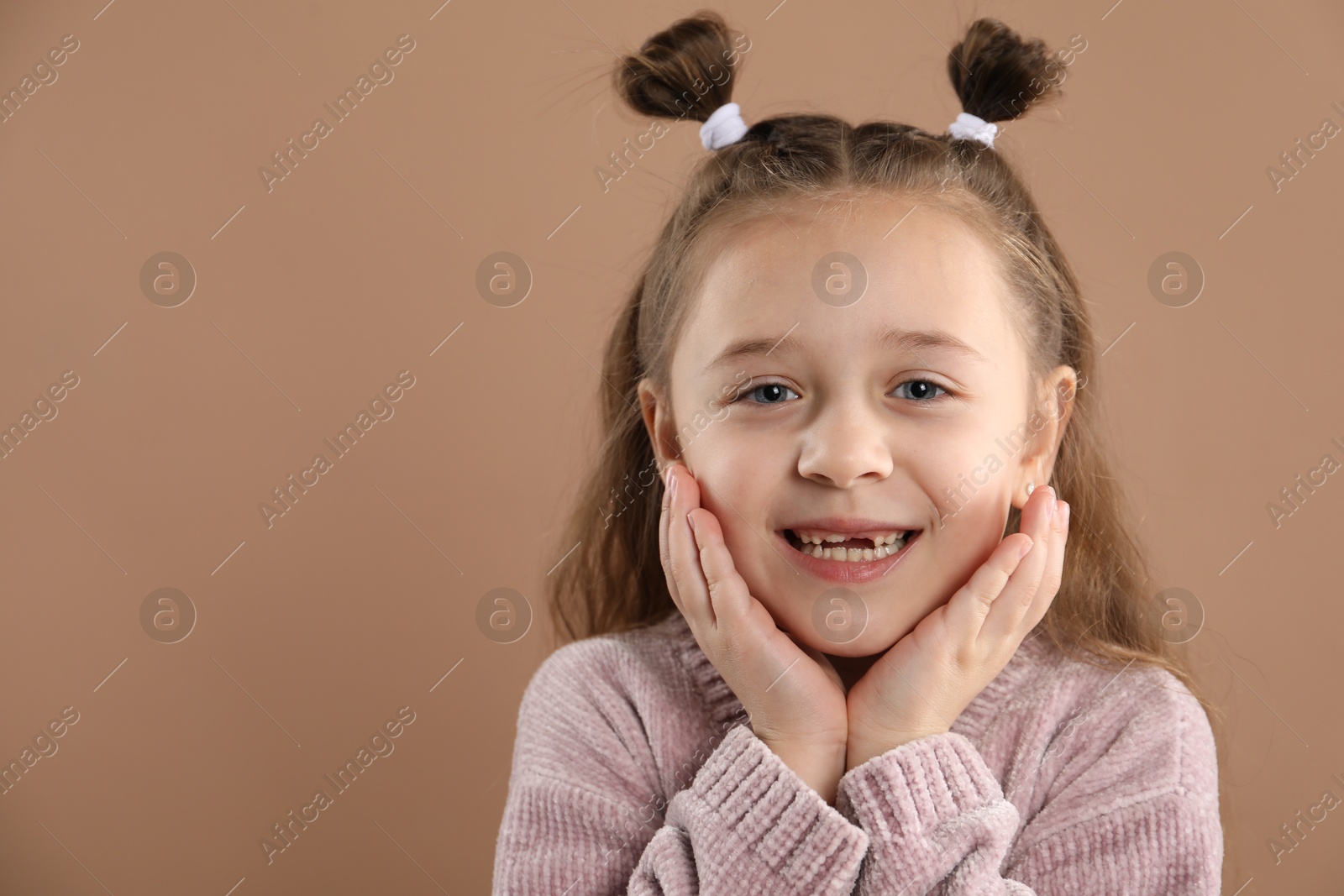 Photo of Portrait of cute little girl with missing tooth on light brown background, space for text