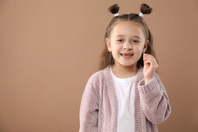 Photo of Cute little girl with missing tooth on light brown background, space for text. Waiting for tooth fairy