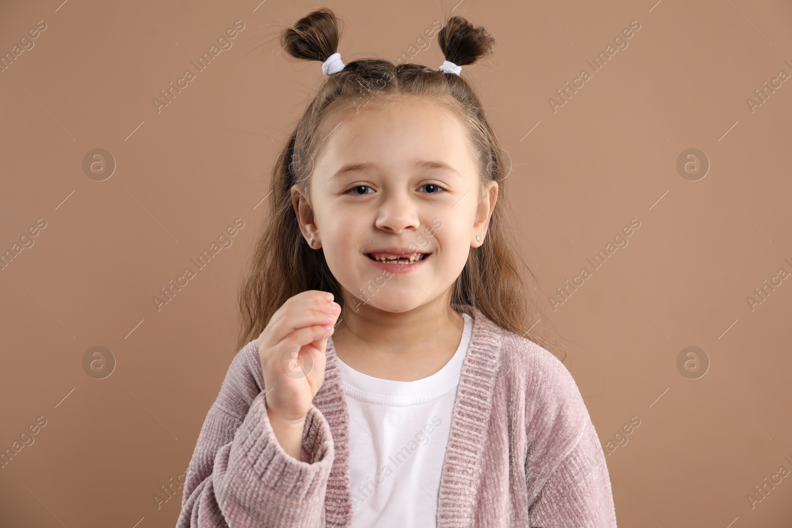 Photo of Cute little girl with missing tooth on light brown background. Waiting for tooth fairy