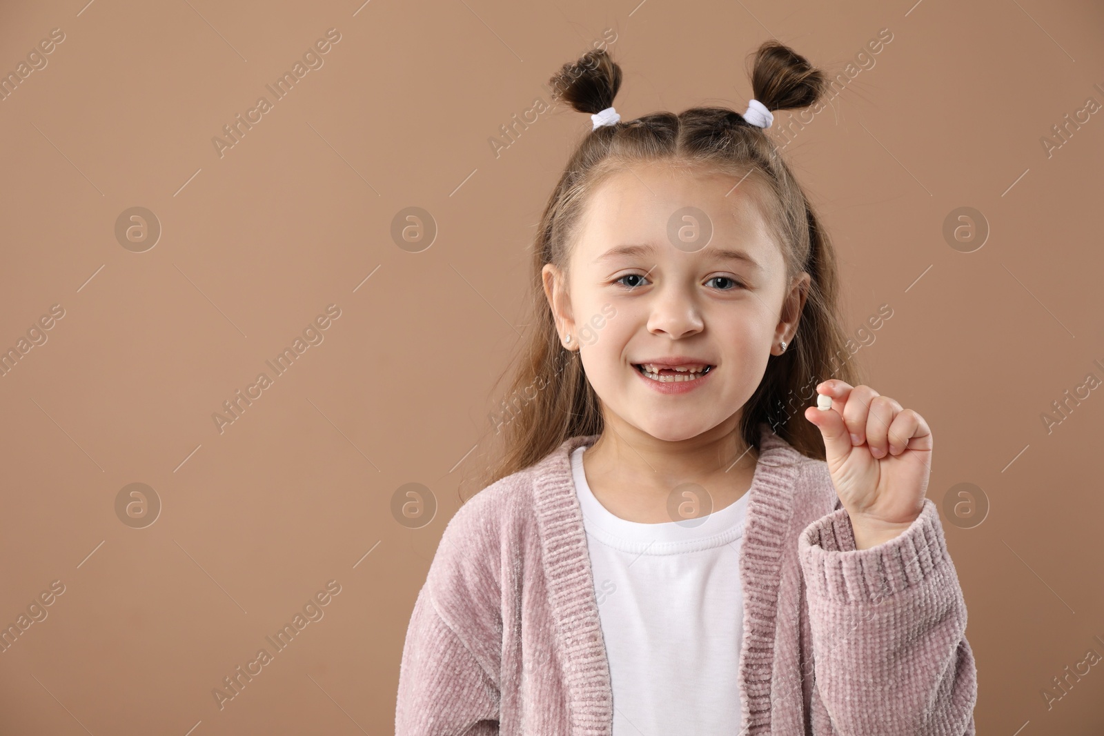 Photo of Cute little girl with missing tooth on light brown background, space for text. Waiting for tooth fairy