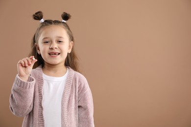 Photo of Cute little girl with missing tooth on light brown background, space for text. Waiting for tooth fairy