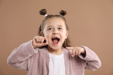 Photo of Cute little girl pointing at her missing tooth on light brown background. Waiting for tooth fairy