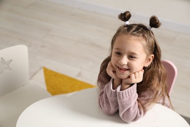 Photo of Cute little girl with missing tooth at white table indoors, space for text