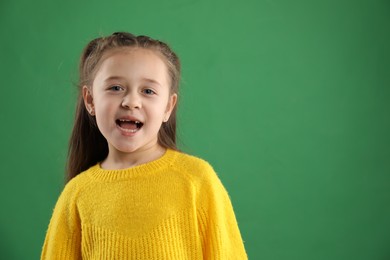 Photo of Portrait of cute little girl with missing tooth on green background, space for text