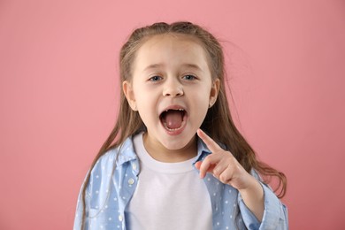 Photo of Cute little girl pointing at her missing tooth on pink background. Waiting for tooth fairy