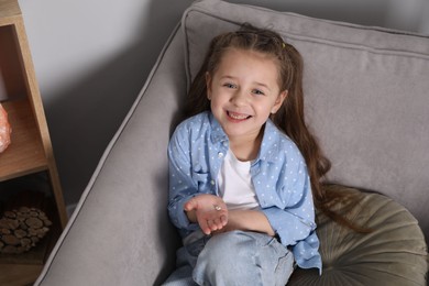 Photo of Cute little girl with missing tooth in armchair at home, above view. Waiting for tooth fairy