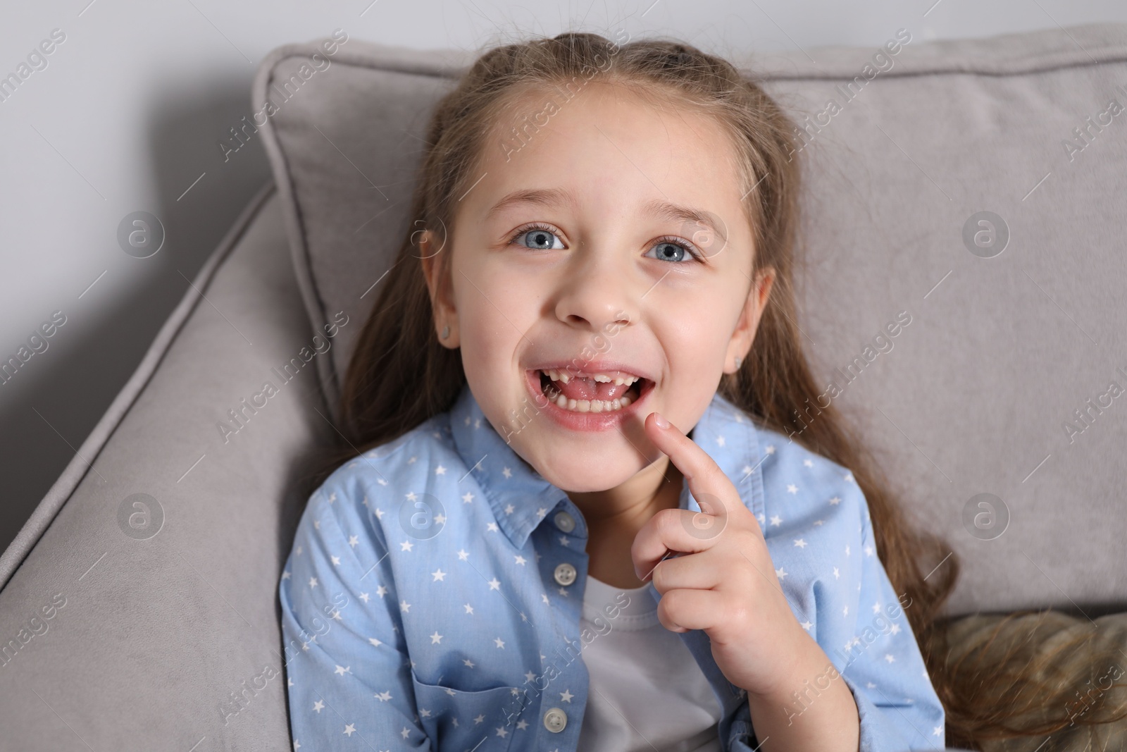 Photo of Cute little girl pointing at her missing tooth in armchair. Waiting for tooth fairy