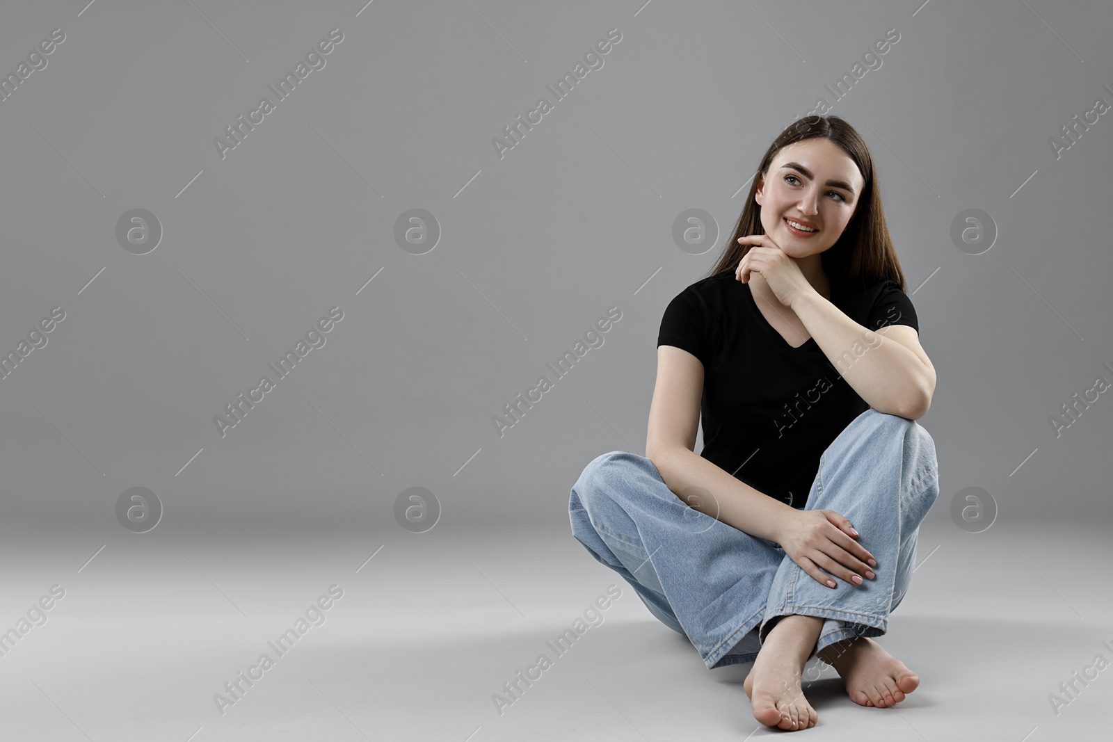 Photo of Smiling woman in stylish jeans on grey background. Space for text