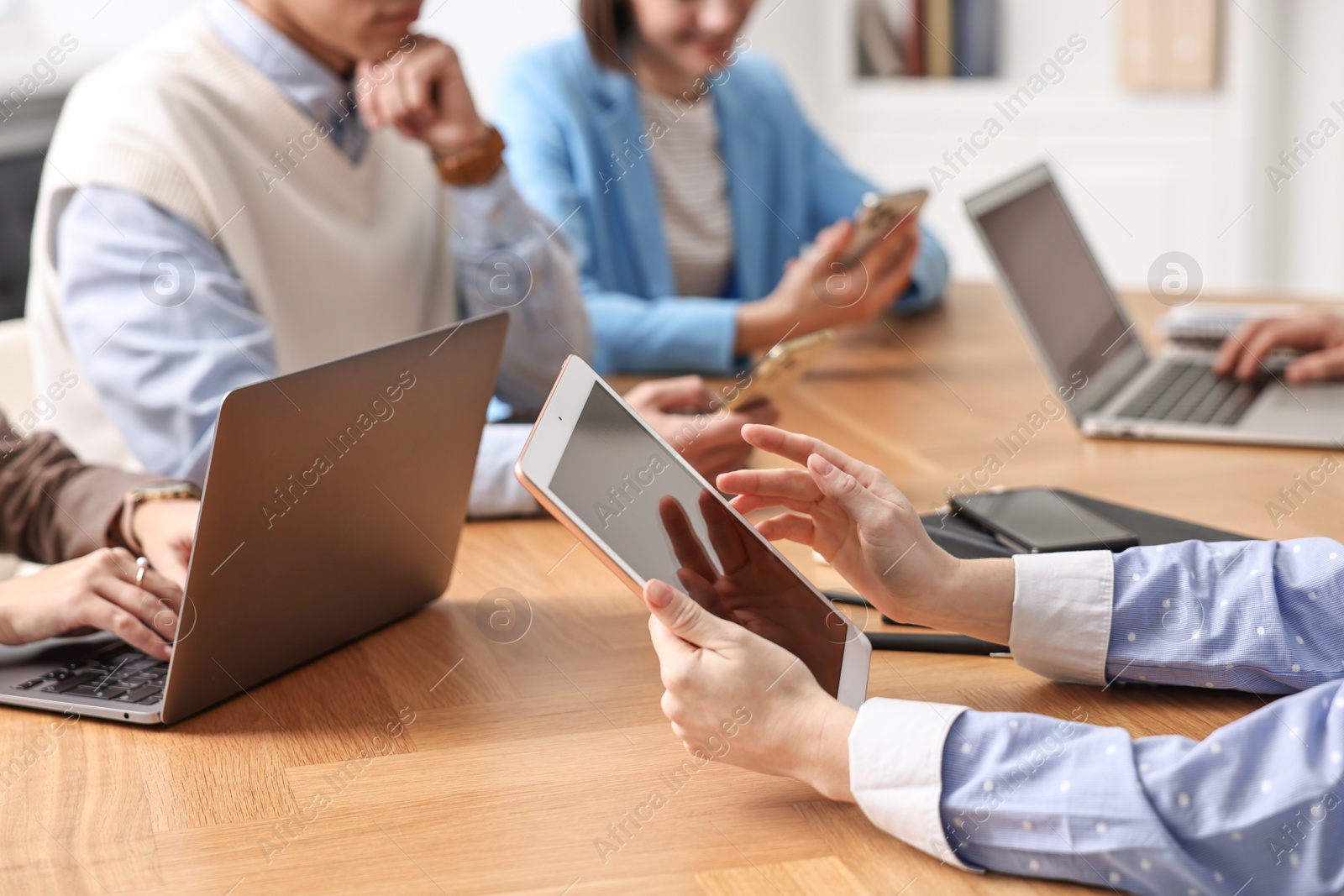 Photo of Group of people using different gadgets at wooden table in office, closeup. Modern technology