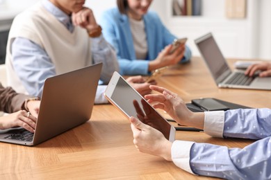 Photo of Group of people using different gadgets at wooden table in office, closeup. Modern technology