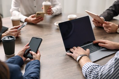 Photo of Group of people using different gadgets at wooden table in office, closeup. Modern technology