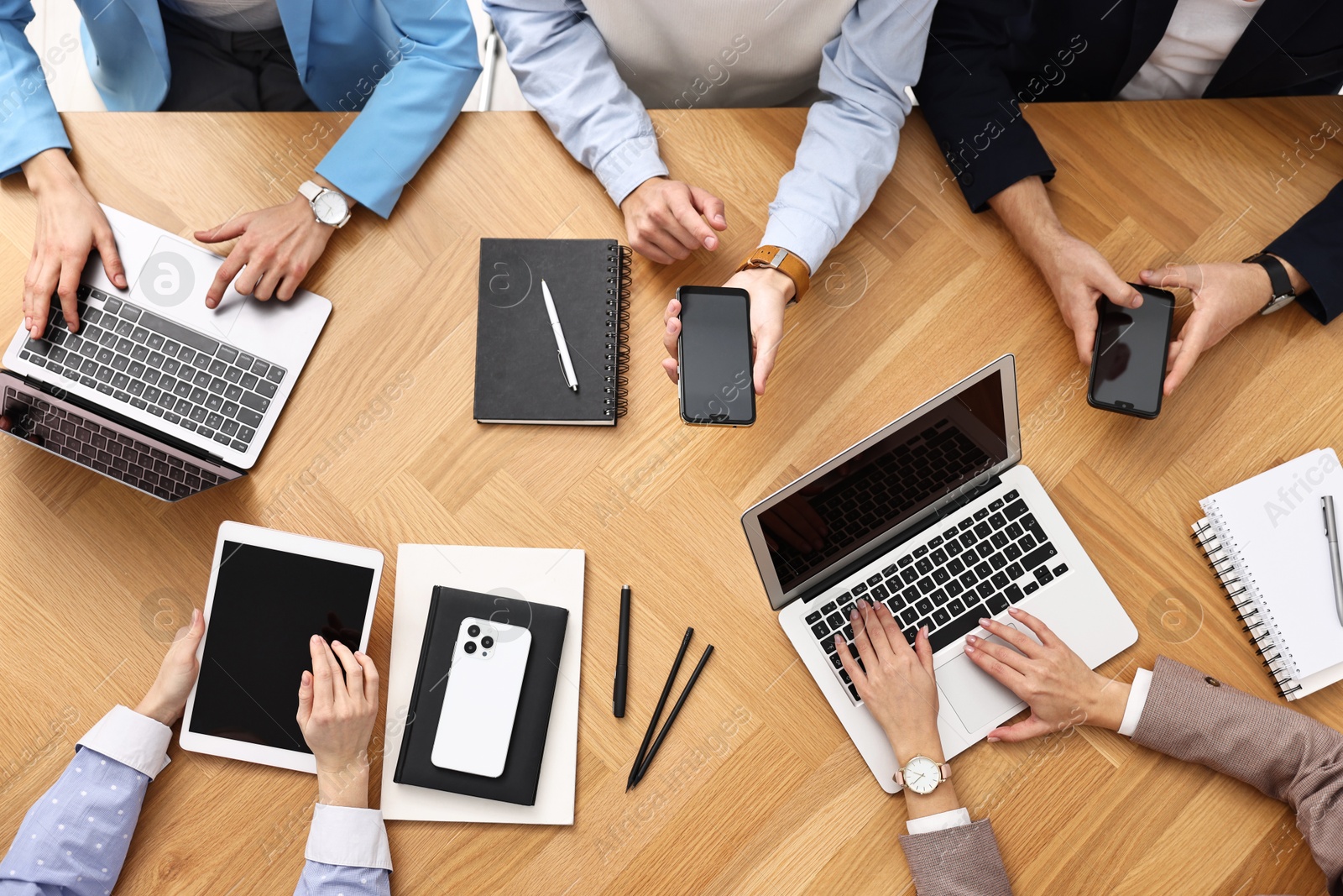 Photo of Group of people using different gadgets at wooden table in office, top view. Modern technology