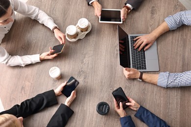 Group of people using different gadgets at wooden table in office, top view. Modern technology