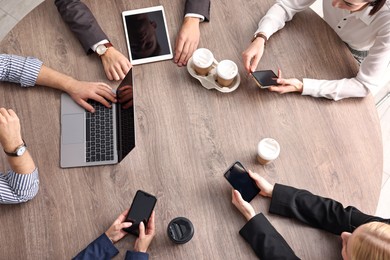 Group of people using different gadgets at wooden table in office, top view. Modern technology