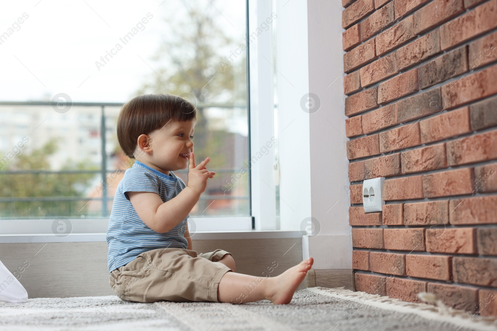 Photo of Little boy sitting near electrical socket at home. Child in danger