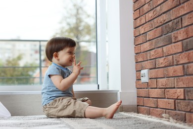 Photo of Little boy sitting near electrical socket at home. Child in danger