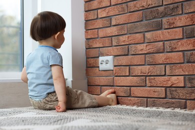 Photo of Little boy sitting near electrical socket at home, space for text. Child in danger