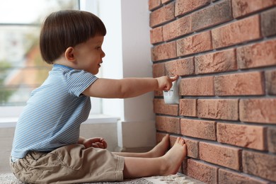 Photo of Little boy playing with electrical socket at home. Child in danger