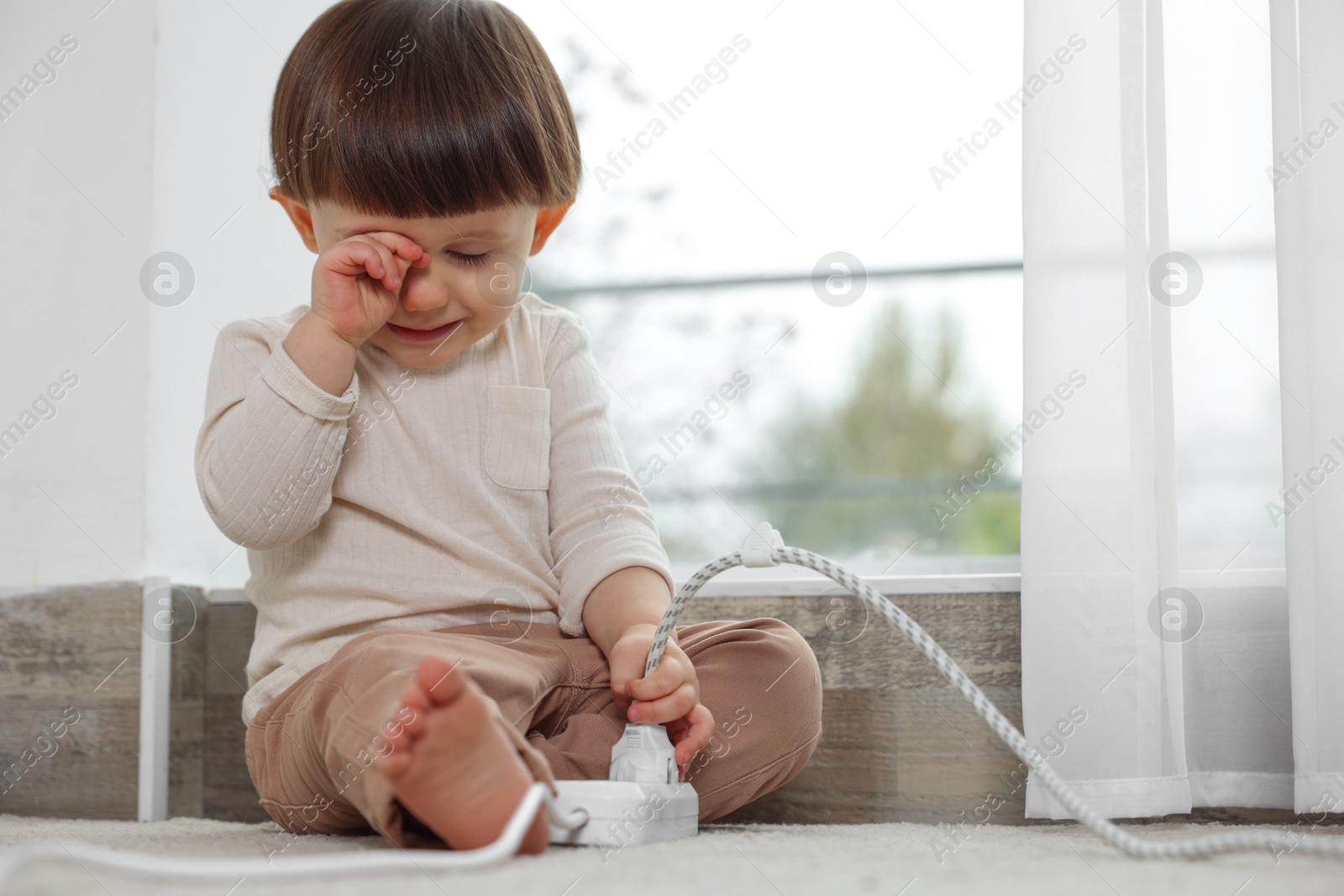 Photo of Little boy crying near iron plug and power strip at home. Child in danger