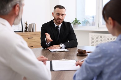 Man and woman having meeting with professional notary at wooden desk indoors