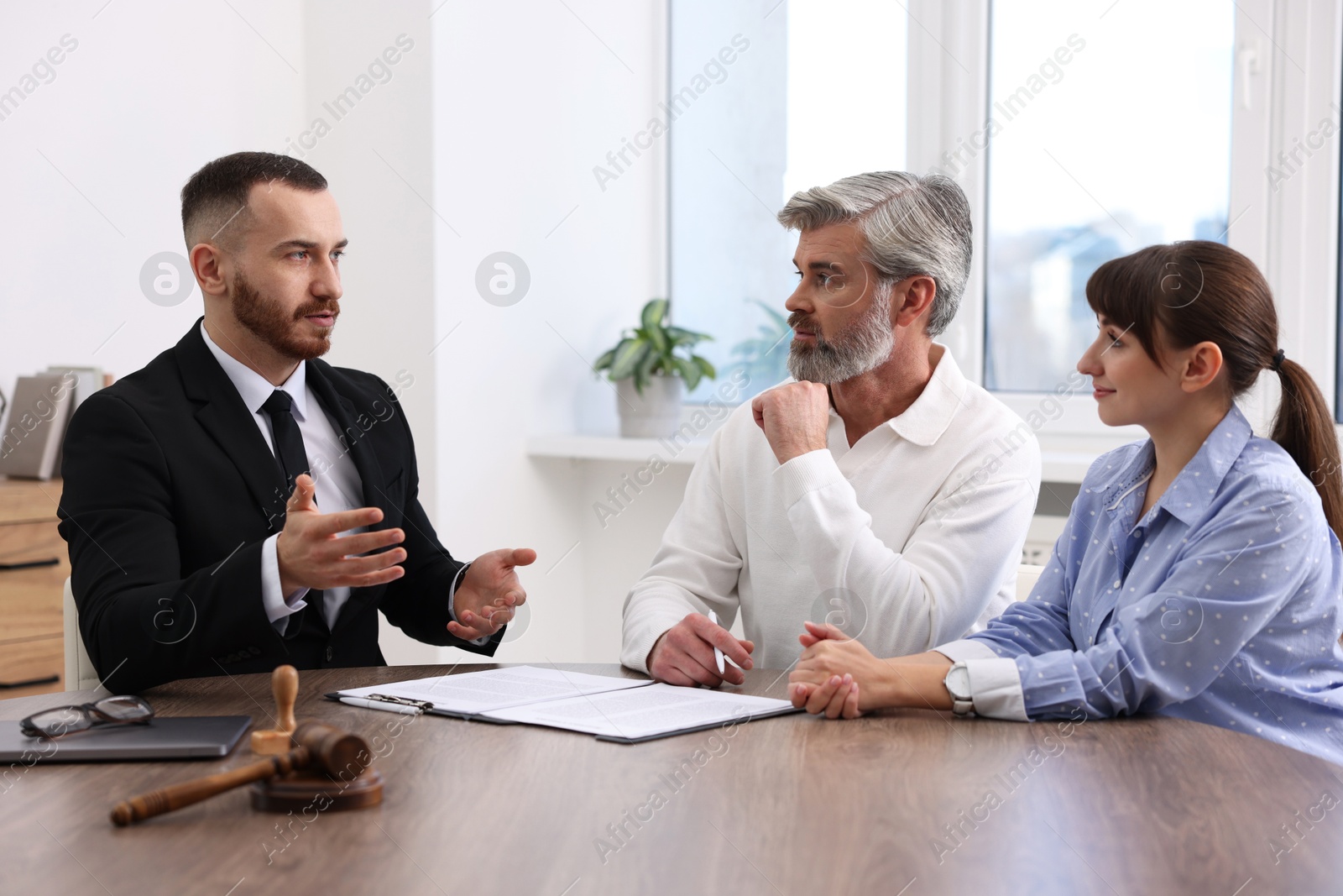 Photo of Couple having meeting with professional notary at wooden desk indoors