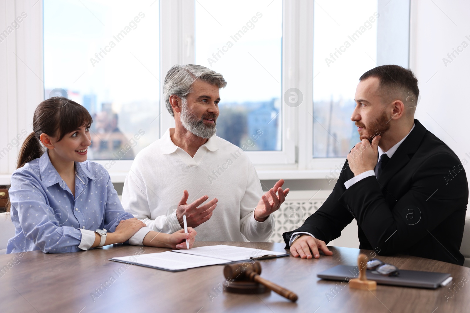 Photo of Couple having meeting with professional notary at wooden desk indoors