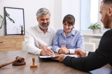 Clients signing notarial paperwork during meeting with lawyer at wooden desk indoors