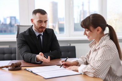 Client signing notarial paperwork during meeting with lawyer at wooden desk indoors, selective focus