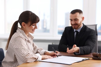 Client signing notarial paperwork during meeting with lawyer at wooden desk indoors, selective focus