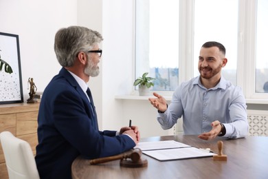 Man having meeting with professional lawyer at wooden desk indoors